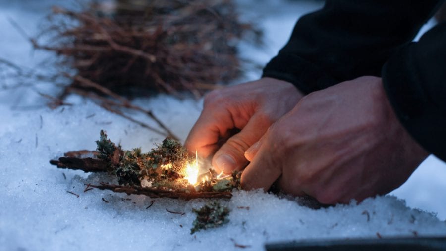 man setting up fire with a firestarter on snowy surface