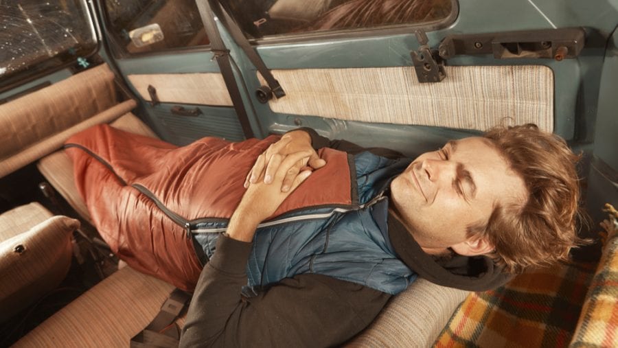 man tucked in a sleeping bag liner preparing to sleep in a car