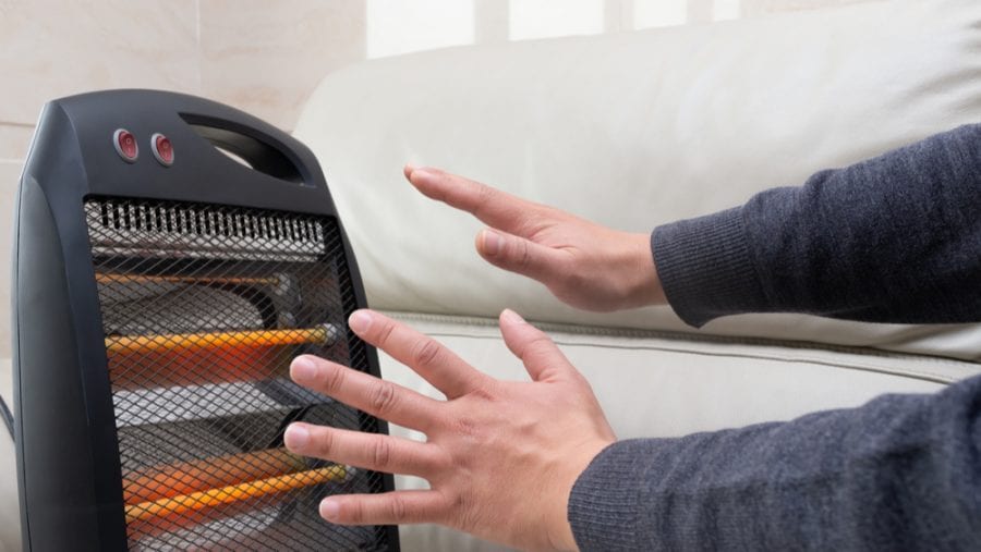 man warming up his hands on a portable electric heater