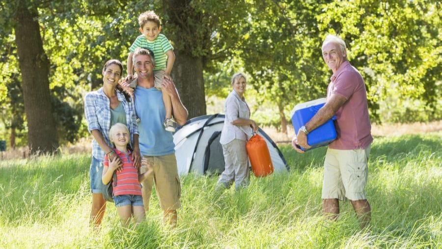 senior carrying blue camping cooler with family