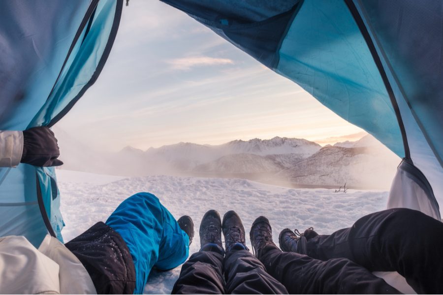 friends camping inside a tent watching a blizzard passing by